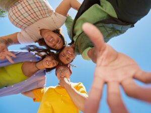 2 ragazze e 2 ragazzi che sorridono e si divertono insieme, inquadrati dal basso verso l'alto. Sopra di loro il cielo azzurro!